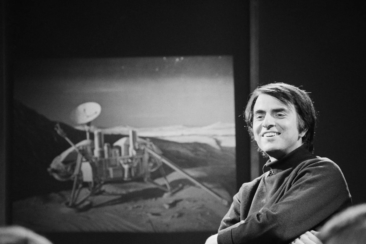 Carl Sagan in a studio with a spacecraft image behind him